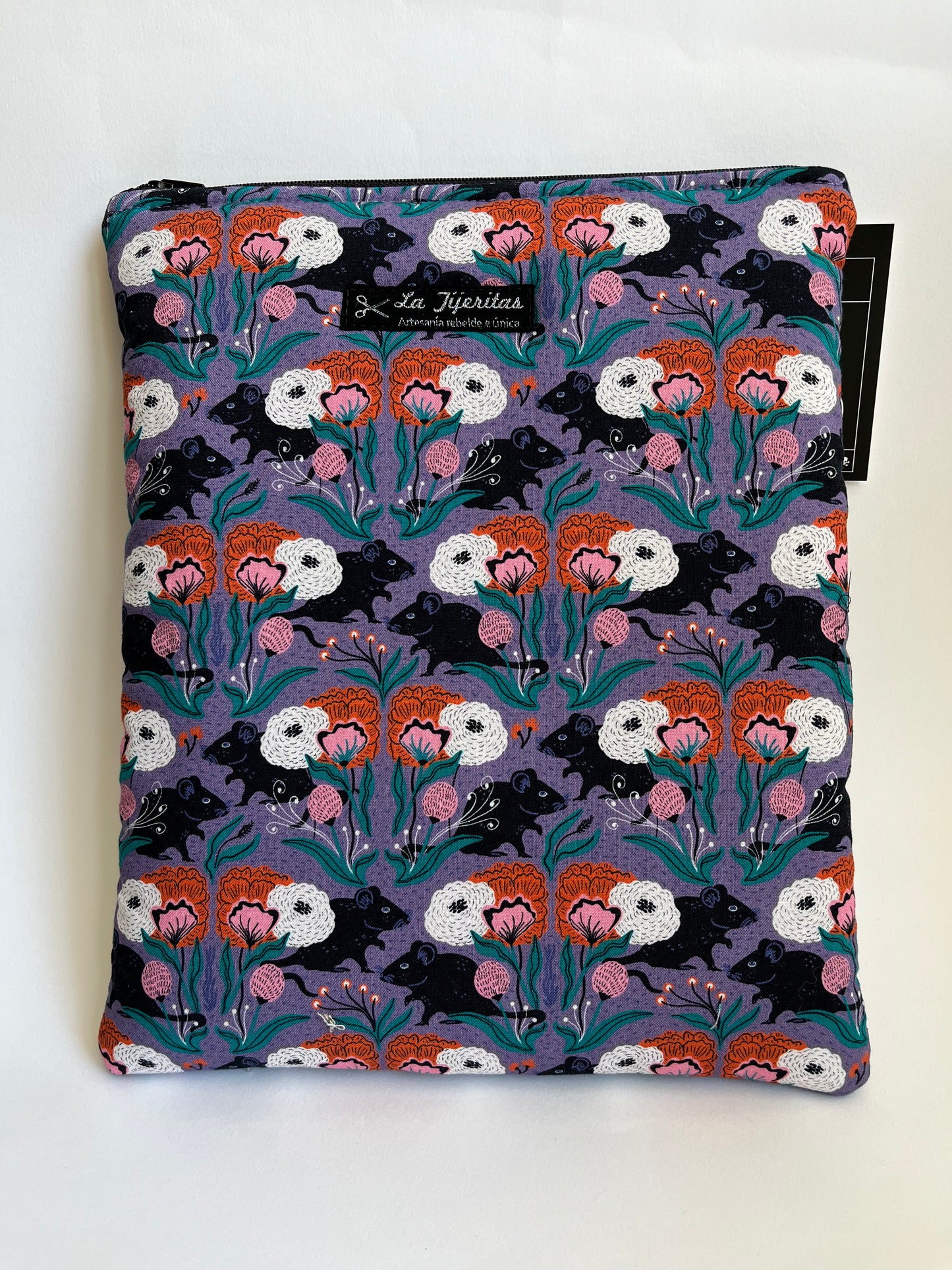 Funda de libro con cremallera, estampado de ratitas negras y flores de color naranja y rosa.
El fondo del estampado es de color lila.
Tiene tiras a contraste de color negro.