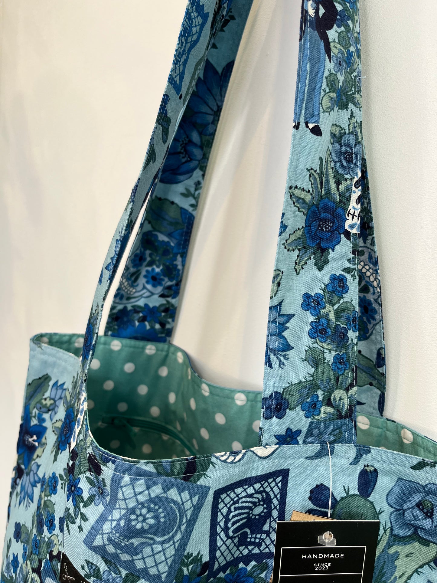 Detalle de las asas de la tote bag, donde se ve que son anchas, también se puede ver el interior, donde se aprecia el forro de lunares verde agua y blanco que hace un contraste muy bonito con la tela exterior.