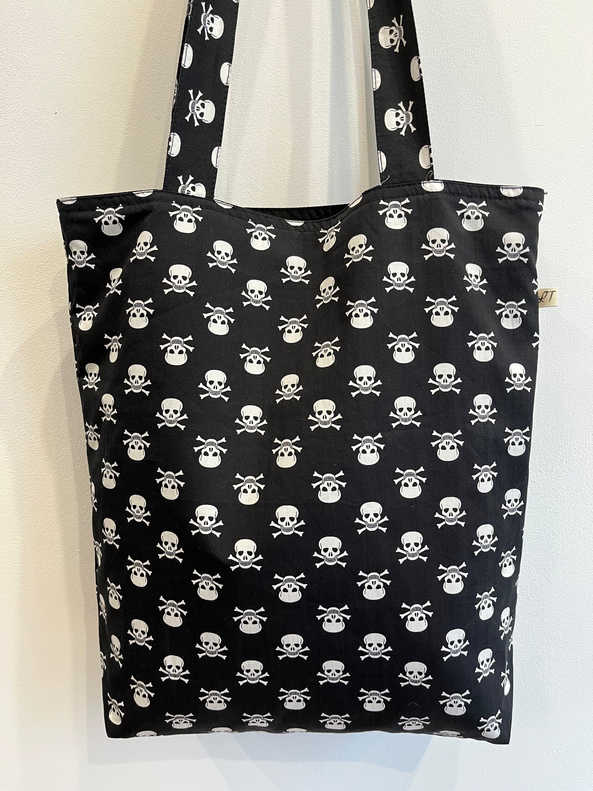 Bolso de tela negra con estampado de calaveras blancas y huesos cruzados en patrón repetitivo.