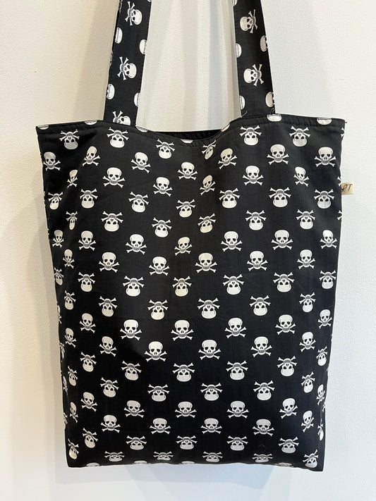 Bolso de tela negra con estampado de calaveras blancas y huesos cruzados en patrón repetitivo.