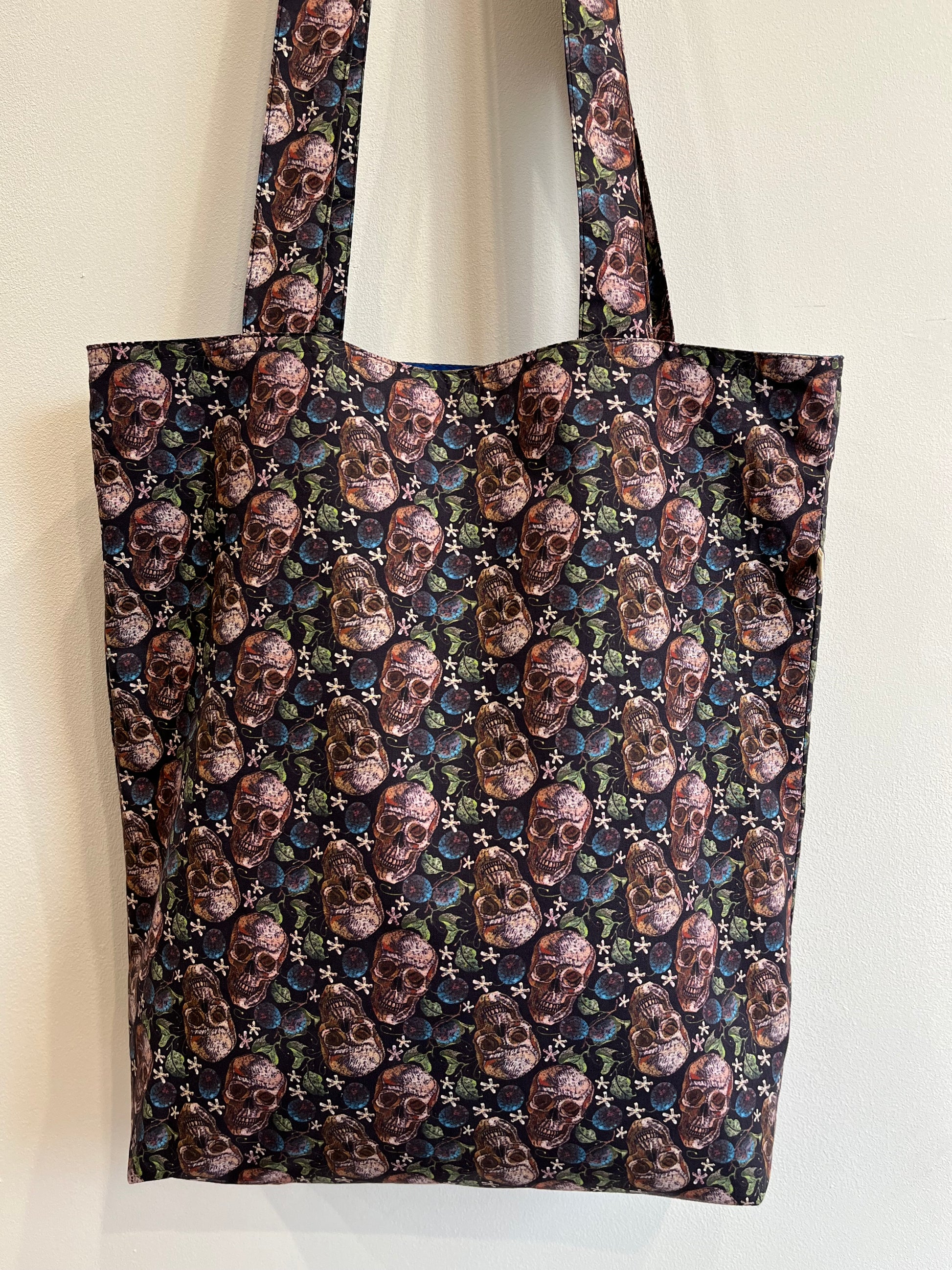 Bolso de tela negra con estampado de calaveras vintage y detalles florales en tonos oscuros.