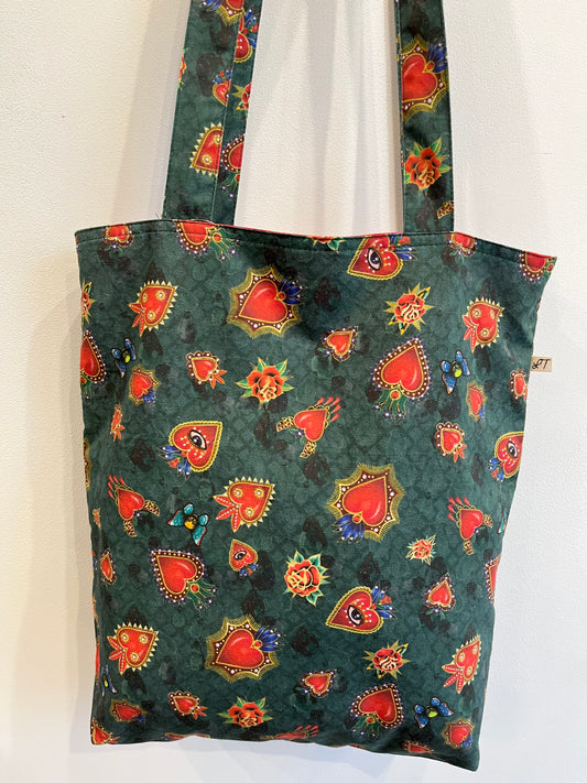 Bolso de tela verde con estampado de corazones rojos, ojos, rosas y mariposas en tonos vibrantes.