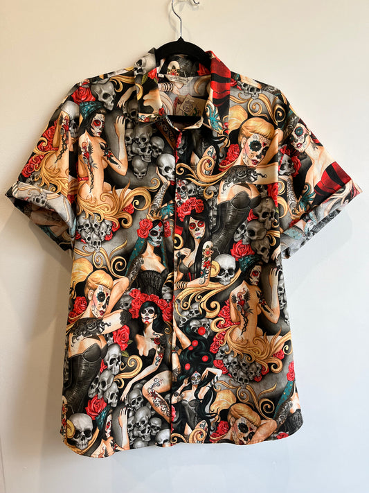 Camisa de manga corta con estampado de mujeres estilo pin-up, calaveras y rosas rojas en tonos oscuros.