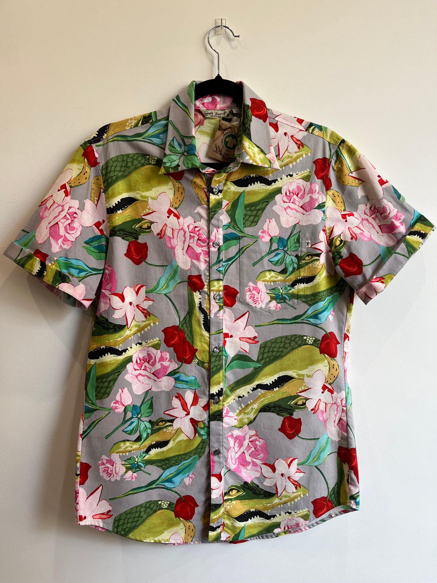 Camisa de manga corta con estampado de cocodrilos verdes y flores rosas y rojas sobre fondo gris.