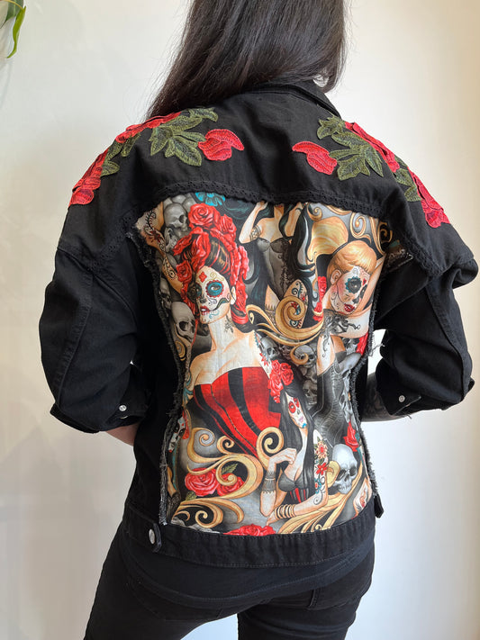 Chaqueta negra personalizada con parche de mujeres estilo pin-up, calaveras y rosas en la espalda, y bordados de rosas rojas en los hombros.