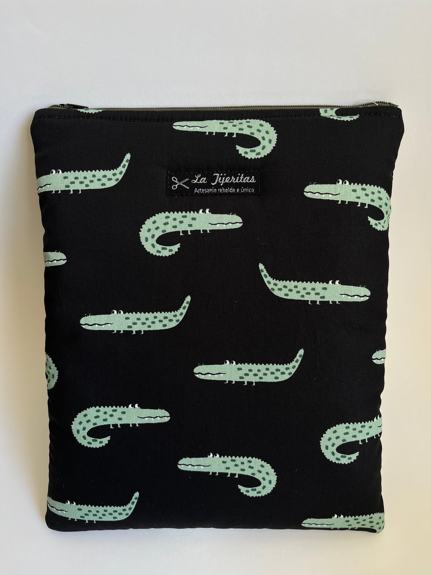 Funda de libro de color negro  con estampado de cocodrilos verdes, con ojos saltones y dientecitos. Correas verde militar a contraste.