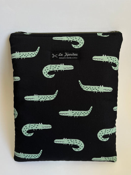 Funda de libro de color negro  con estampado de cocodrilos verdes, con ojos saltones y dientecitos. Correas verde militar a contraste.