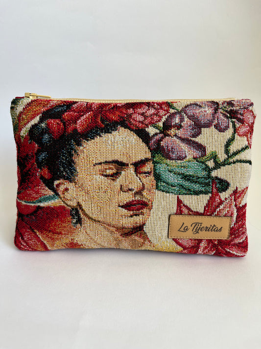 Neceser de tamaño pequeño, como medio  folio, en tonos beige, granate y malva. Tiene la cara de Frida Khalo.