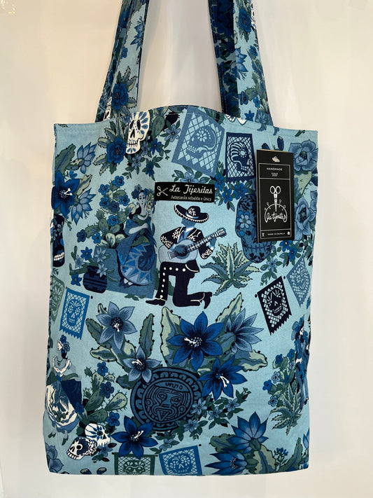 Tote bag artesanal con estampado mexicano de flores y mariachis tocando, en tonos azules. Es de algodón orgánico y tiene un bolsillo con cremallera dentro.