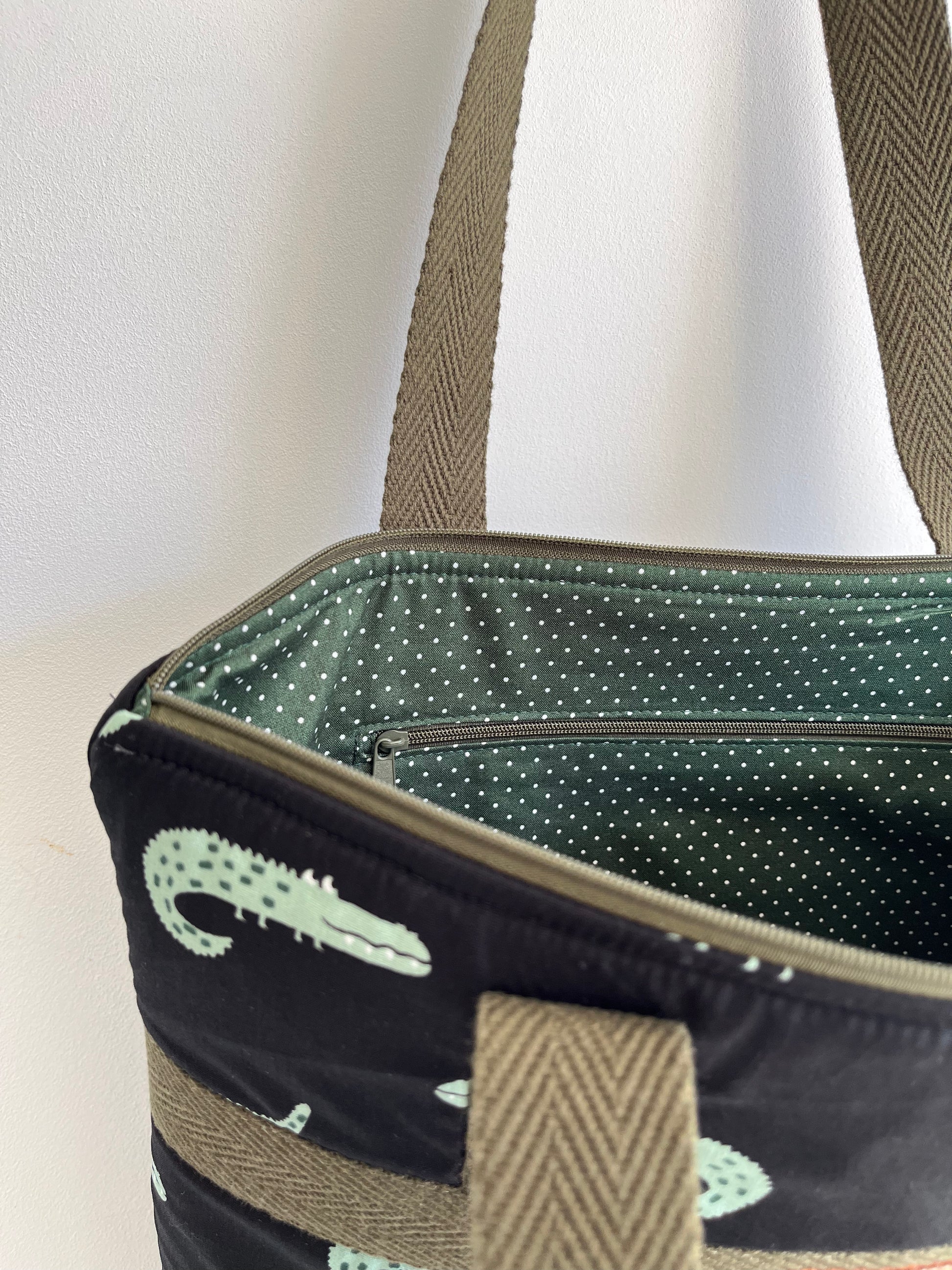 Detalle de la esquina del bolso donde se ve el bolsillo interior con cremallera. El  forro es verde con topitos blancosl.