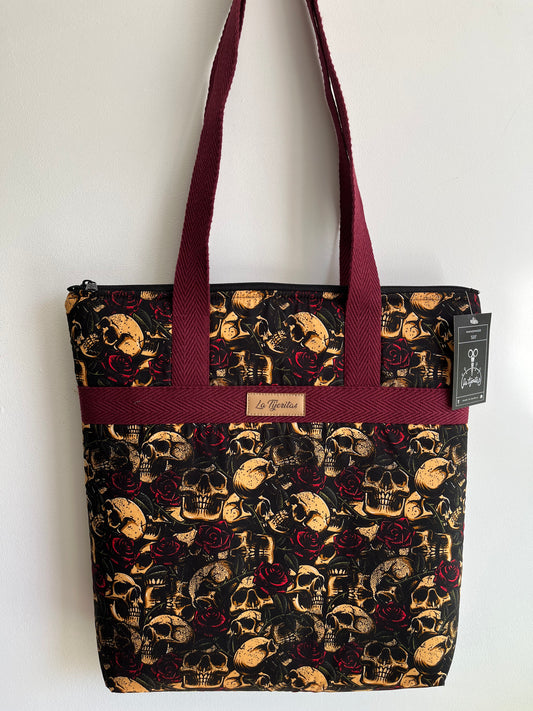 Bolso de color negro con calaveras beige y rosas rojo oscuro. Tiene tiras a contraste de color vino.