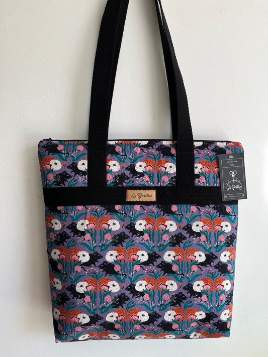 Bolso con estampado de ratitas negras y flores de color naranja y rosa. 
El fondo del estampado es de color lila.
Tiene tiras a contraste de color negro.